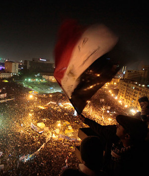 An Egyptian waves the national flag as he and others watch thousands ...