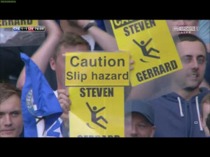 Chelsea fans hold up Caution:Slip Hazard posters for Steven Gerrard