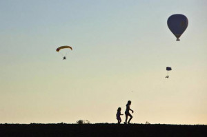 Children are silhouetted as a hot air balloon (R) and paragliders fly ...