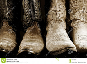 Two pairs of well worn cowboy boots in high contrast light.