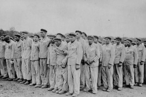 Prisoners standing during a roll call. Each wears a striped hat and ...