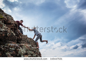 Man giving helping hand to friend to climb mountain rock cliff