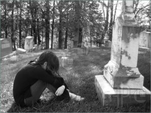 ... girl mourning in a graveyard, curled up in front of a large grave