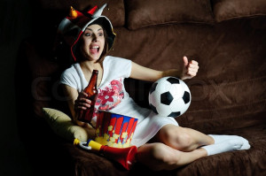 Stock image of 'An image of a girl on a sofa watching football on TV'