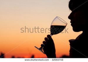 Woman drinking a glass of wine by the sunset - stock photo