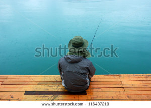 Man sitting at jetty fishing near lake during rainy day - stock photo