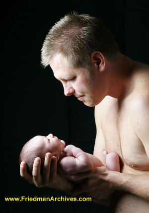 fatherholds his newborn baby in formal portrait with dramaticlight.