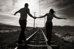 Young couple walking hand in hand on train track, rear view (B&W)