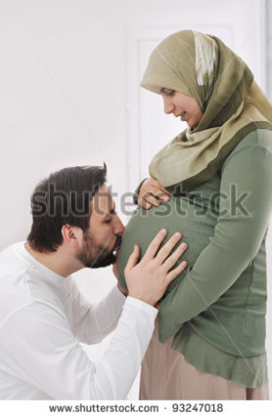 Pregnant muslim wife smiling with her husband kissing belly,and his