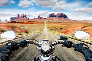 Man riding motorcycle on dirt track, Monument valley in background