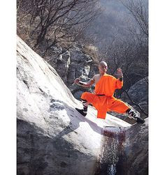 Shaolin monk dressed in traditional orange robe practicing on stones ...