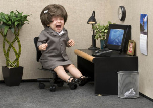 Female toddler dressed in suit sitting at office desk crying.