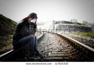 ... girl with hands over her face sitting on the railroad - stock photo