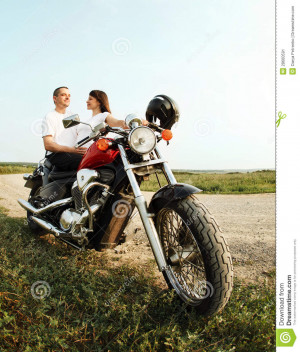 Young biker couple on the country road against the sky.