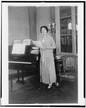 Alma Gluck full length portrait standing by piano facing slightly