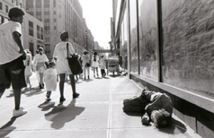man lying on sidewalk as people pass by