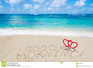 Sign Good morning with two hearts on the sandy beach by the ocean.