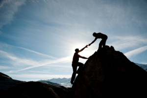 One person helping another climb up a mountain