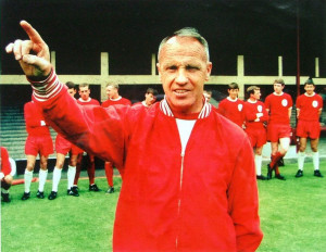 Bill Shankly in a red jacket pointing, with players in the background.