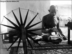 Mahatma Gandhi sitting beside his spinning wheel,
