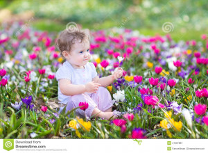Stock Photo: Cute curly little baby sitting between spring flowers
