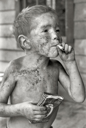 Boy covered by dirt smoking cigarette with one hand, holding can of ...