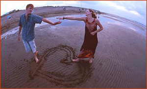 ... happy couple at the beach holding hands. Heart drawing in the sand