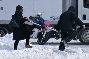 man helps a woman carry a child in a stroller through a snow covered ...