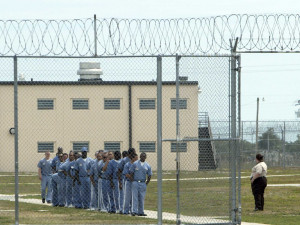 Inmates stand in line under the watchful eye of a corrections officer ...