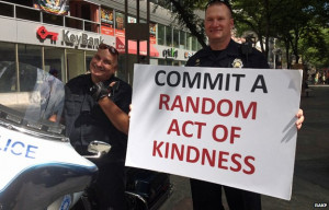 Police Officers Hold A Sign That Says Commit A Random Act Of Kindness.