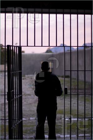 of a man, at sunset, exiting through the iron bars into the prison ...