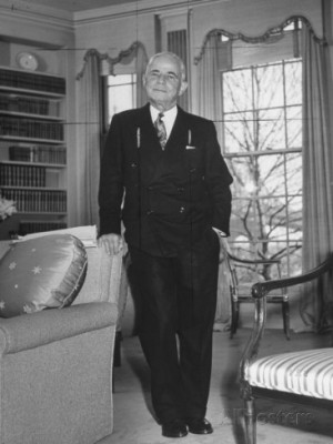 Broker Charles E Merrill Standing in Living Room with Hand Resting on