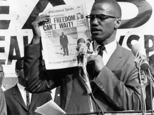 Black Muslim leader Malcolm X holds up a paper for the crowd to see ...
