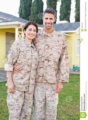 Military Couple In Uniform Standing Outside House Smiling.