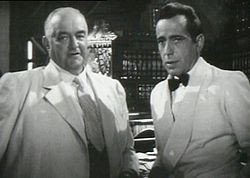 Black-and-white film screenshot of two men, both wearing suits. The ...