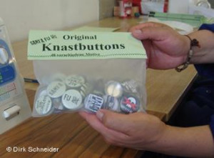 ... holding bag of buttons with sayings about prison life printed on them