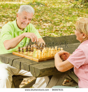 Happy elderly couple has fun playing chess in the park. - stock photo