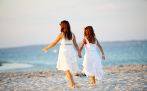 Two little girls walking on the beach hand by hand