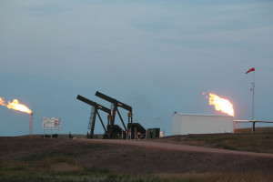 photo of large flares coming from stacks near oil well pumps