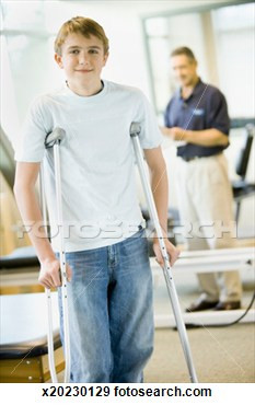 of Teenage boy (14-16) with crutches, physical therapist in background ...