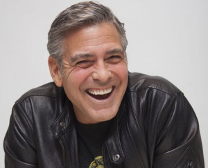 George Clooney laughing in a black leather jacket at press junket