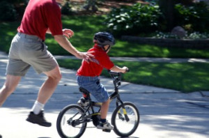 He is teaching his son how to ride a bicycle.