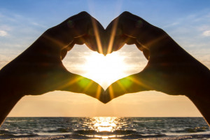 man's hands cradle the sun in the shape of a heart