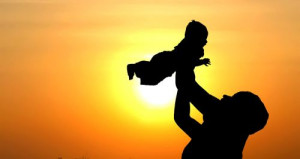 mom holding a baby high up in the air against a sunset backdrop