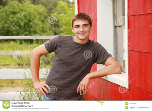 Senior Portrait of a handsome young man leaning against a red barn ...