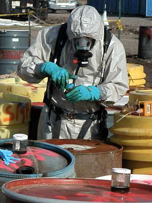 Photo of worker surrounded by metal barrels of chemical waste, in full ...