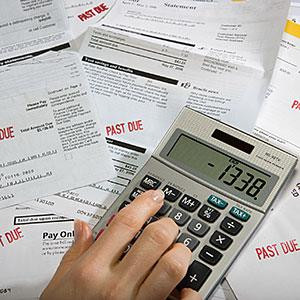 Woman using calculator on desk full of bills and statements © Sheer ...