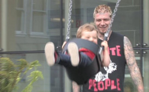 Lars Frederiksen of Rancid pushes his son on a playground swing set.