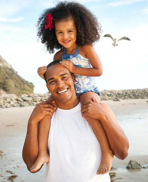 Black father carrying daughter on shoulders on beach