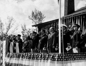Men in suits and uniforms stand on a dais decorated with bunting and ...